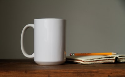 白色的陶瓷杯子旁边开放图书页面上橙色的铅笔

